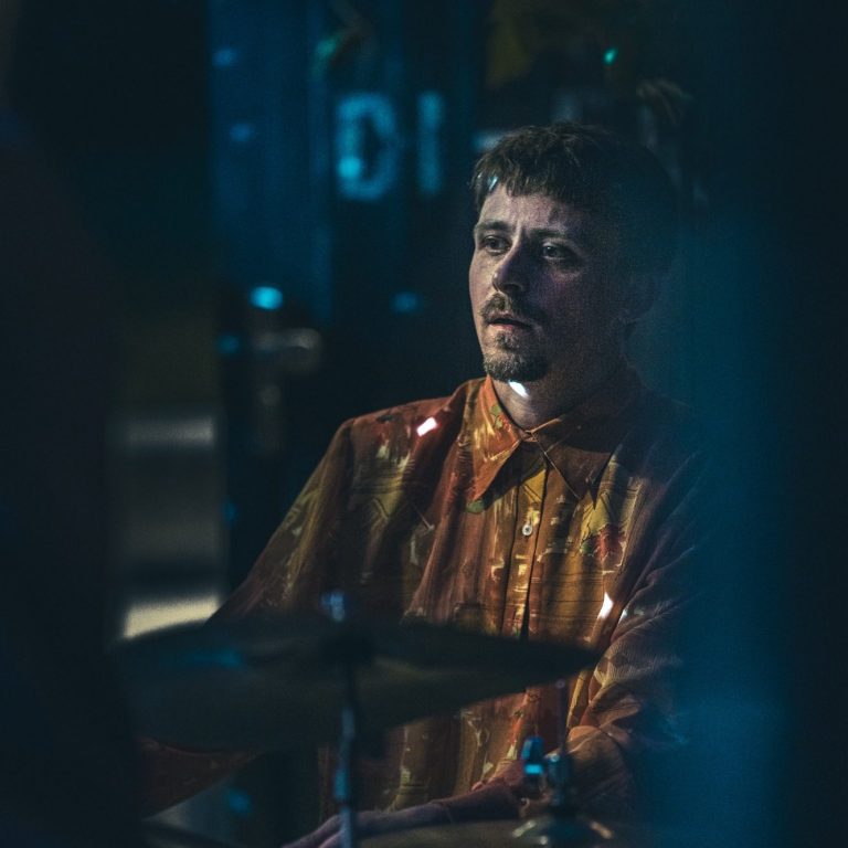 Johannes Bode hochkonzentriert am Schlagzeug in orangefarbenen Shirt